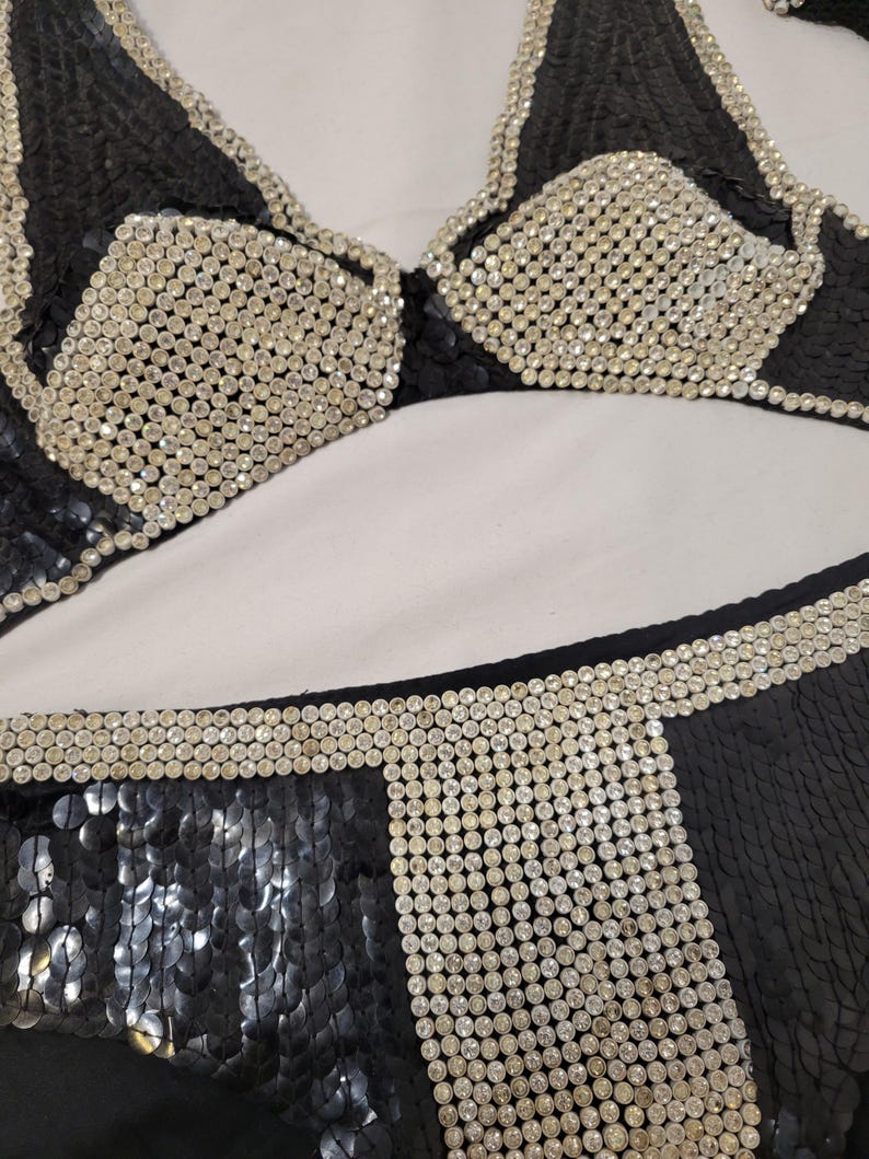 May include: Black sequined bikini set with silver rhinestone accents. The top features a triangle design with rhinestone-covered cups and trim. The bottoms have a sequined design with rhinestone detailing.