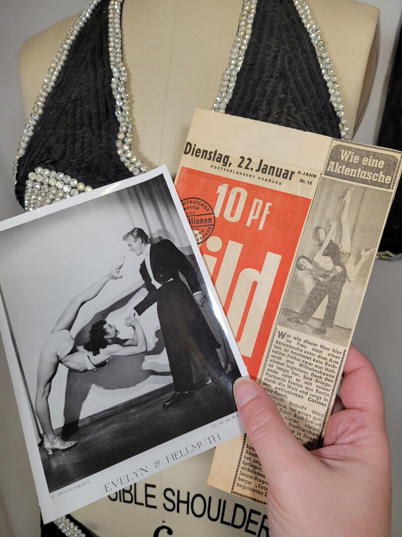 May include: Black halter top with pearl embellishments, vintage photographs, and a newspaper clipping. The photographs feature acrobatic performers. The newspaper is in German and dated January 22.