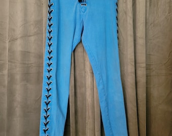 Könnte beinhalten: Hellblaue Jeanshose mit schwarzen Schnürdetails an den Seiten und vorne. Die Hose hängt an einem schwarzen Kleiderbügel. Das Design hat eine schmale Passform. Der Hintergrund ist neutral gefärbt.