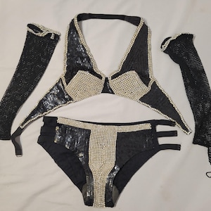 May include: A black sequined bikini set with pearl accents, including a halter top, high-waisted bottoms, and two long gloves. The bikini top and bottoms feature pearl detailing. The gloves are made of a black mesh material.