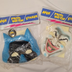 May include: Two plastic Halloween masks, one blue and black Batman mask and one white Joker mask, packaged together in a plastic bag with a sticker that reads "Mask Photo Button Sticker 3PC Action Set".