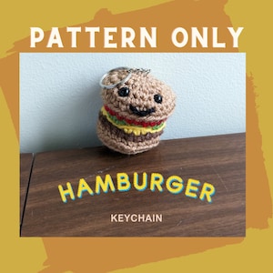 Könnte beinhalten: Häkelanleitung für einen Hamburger-Schlüsselanhänger. Die Anleitung enthält Anweisungen zum Herstellen eines braunen Hamburgers mit gelbem Käse, grünem Salat und roter Tomate. Der Schlüsselanhänger ist an einem silbernen Schlüsselring befestigt.