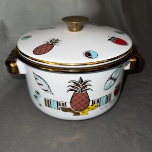 May include: White enamel pot with lid, featuring a gold rim and handle accents. The pot is decorated with colorful pineapple and abstract designs. The lid has a gold knob. The pot has two handles.