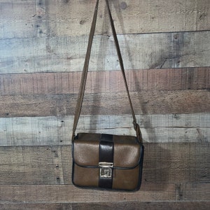 May include: A brown leather shoulder bag with a black stripe and a gold clasp.