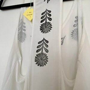 May include: White tank top with black floral and leaf print. The back features a central panel with two large flower designs and leaf accents. The top has a tag that says "I am upcycled".