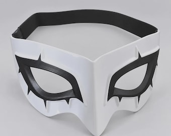 May include: A white plastic mask featuring sharp, angular black eye cutouts with pointed edges. The mask has a rigid, molded structure and includes a wide, black elastic strap attached to the sides for securing it around the head.