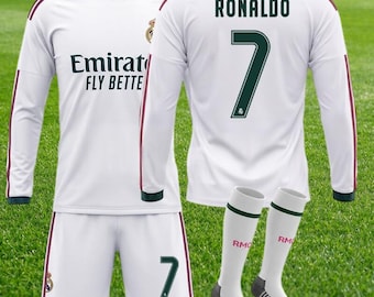 以下が含まれることがあります： ダークグリーンのアクセントが入った白い長袖サッカーユニフォーム。Emirates Fly Betterの文字、Ronaldoの名前、背番号7がプリントされています。背番号7が入った白いショートパンツと、RMCFの文字が入った白いサッカーソックスがセットになっています。
