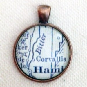 May include: A copper-toned pendant featuring a vintage map of Corvallis, Oregon. The map shows the town's streets and surrounding areas, including the names "Whittier" and "Hami".