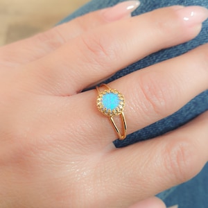 Peut inclure: Une bague en or avec une opale bleue sertie dans un design délicat et orné.