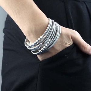 Puede incluir: Un conjunto de pulseras plateadas con detalles de cuentas. Las pulseras se llevan en la muñeca.