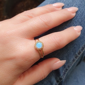 Op de afbeelding: Een gouden ring met een blauwe opaal-steen gezet in een delicate halo van kleinere stenen.
