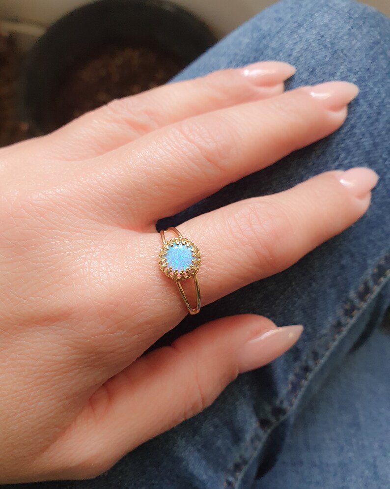 Op de afbeelding: Een gouden ring met een blauwe opaal-steen gezet in een delicate halo van kleinere stenen.