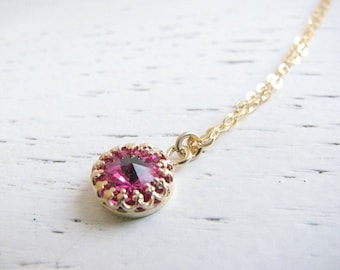 May include: A delicate gold chain necklace with a small, round pendant featuring a pink gemstone surrounded by a gold setting.