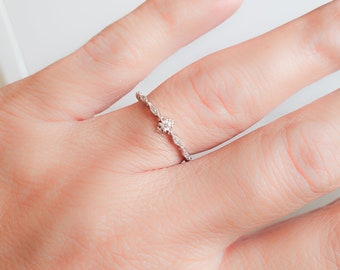 May include: A delicate silver ring with a small, clear stone set in the center. The ring has a twisted band design.