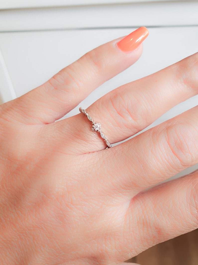 May include: A delicate silver ring with a small, clear stone set in the center. The ring has a twisted band design.