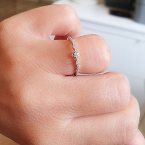 May include: A delicate silver ring with a small, round diamond in the center and smaller diamonds set along the band.