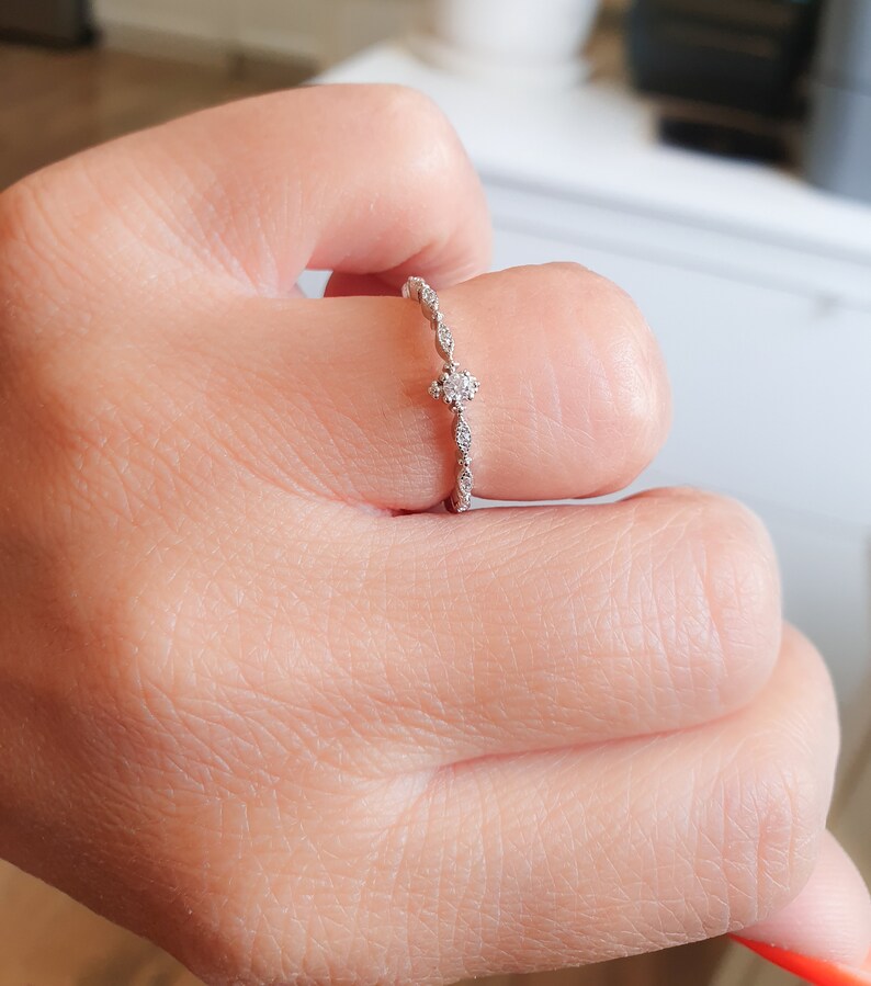 May include: A delicate silver ring with a small, round diamond in the center and smaller diamonds set along the band.
