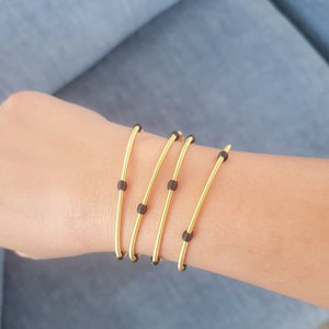 Könnte beinhalten: Vier goldene Armbänder mit schwarzen Perlen am Handgelenk einer Person.
