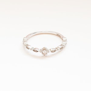 May include: A silver ring with a small, clear stone in the center and a delicate, patterned band.