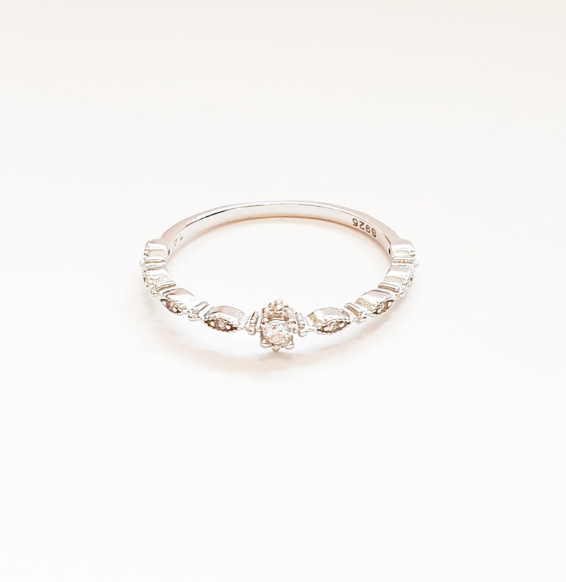 May include: A silver ring with a small, clear stone in the center and a delicate, patterned band.