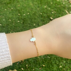 May include: A gold chain bracelet with a white opal hamsa hand charm.