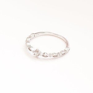 May include: A silver ring with a small, clear stone in the center and smaller stones set around the band.