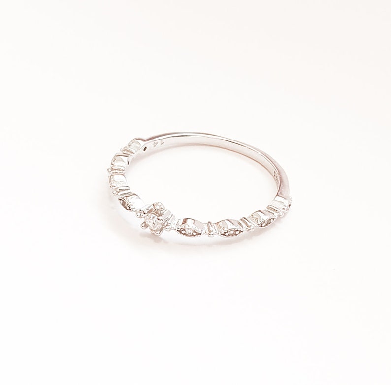 May include: A silver ring with a small, clear stone in the center and smaller stones set around the band.