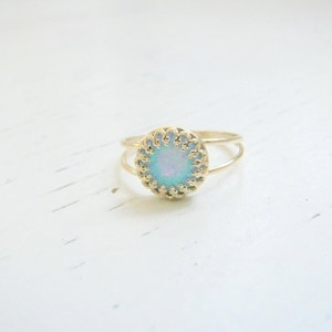 Op de afbeelding: Een delicate gouden ring met een ronde, iriserende opaalsteen gezet in een filigraan ontwerp.