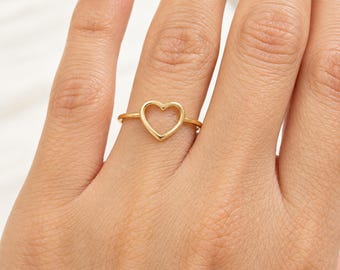 May include: A thin gold ring featuring a simple, open heart-shaped design centered on the band. The metal has a smooth, polished finish, and the heart outline is minimalist in its construction, sitting flat against the finger.