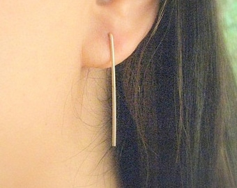 May include: A pair of gold-toned minimalist earrings with a long, thin, straight bar design.