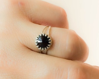 Könnte beinhalten: Ein silberner Ring mit einem schwarzen Kristall, der in einer silbernen Fassung sitzt. Der Ring befindet sich an einem Finger.