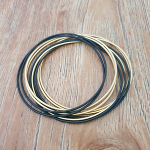 Peut inclure: Un ensemble de bracelets joncs dorés et noirs. Les bracelets sont empilés les uns sur les autres, créant un look superposé.