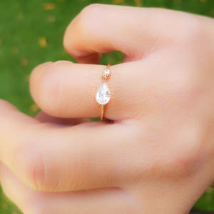 Op de afbeelding: Een gouden ring met twee heldere peervormige stenen. De ring is aan &eacute;&eacute;n kant open en heeft een delicaat ontwerp.