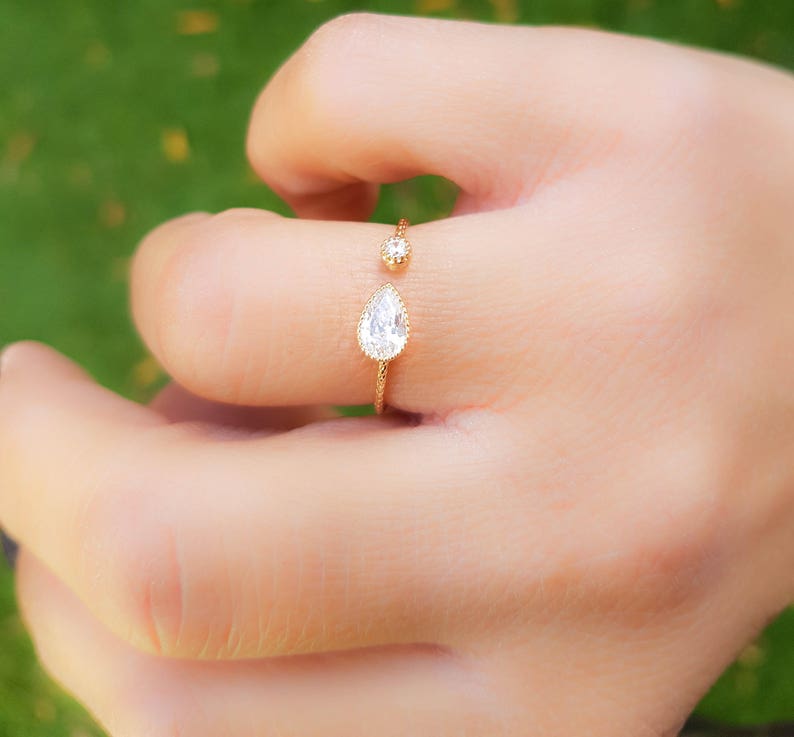 Op de afbeelding: Een gouden ring met twee heldere peervormige stenen. De ring is aan &eacute;&eacute;n kant open en heeft een delicaat ontwerp.