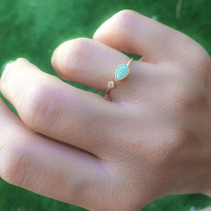 Op de afbeelding: Een gouden ring met een traanvormige groene edelsteen en een kleinere ronde, heldere edelsteen. De ring is open en verstelbaar.