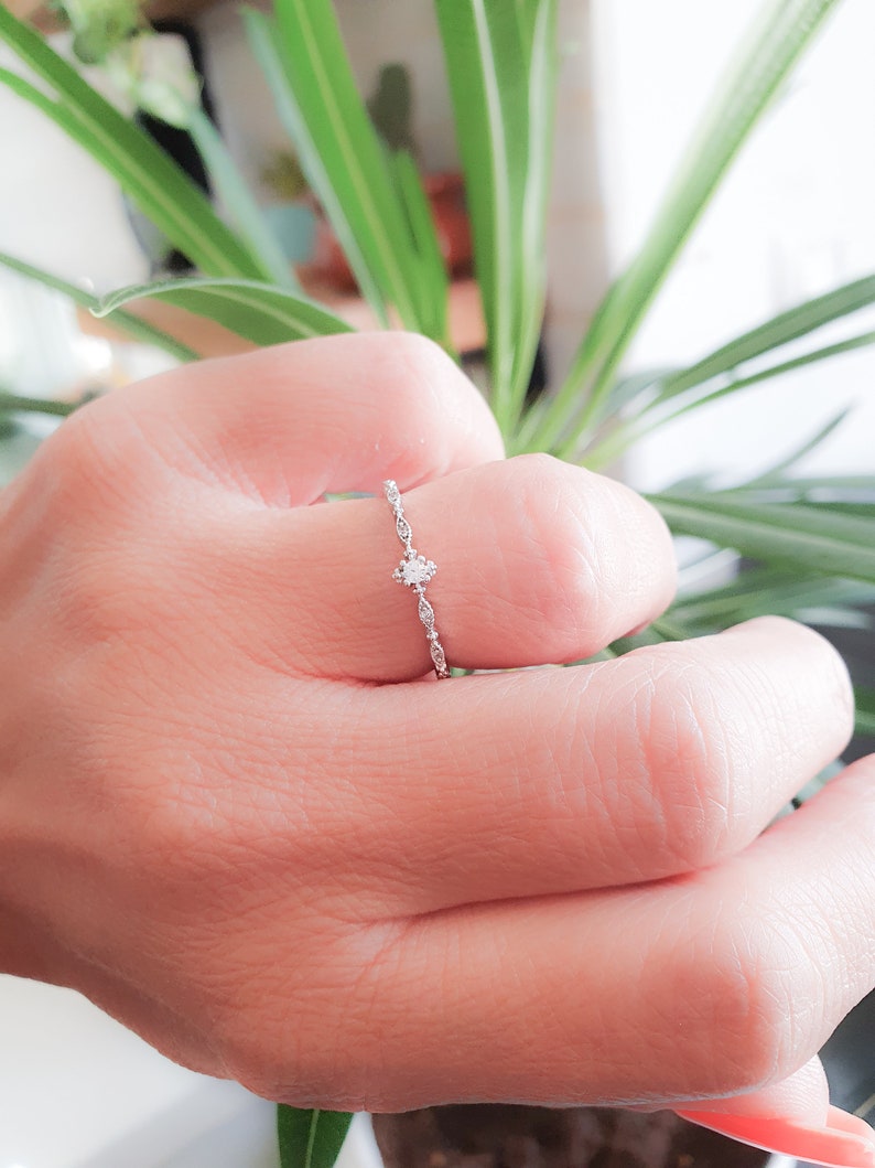 May include: A delicate silver ring with a small, clear gemstone set in the center. The band is adorned with a delicate, intricate design.