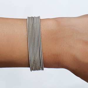 Puede incluir: Un brazalete plateado hecho de múltiples bandas delgadas de metal flexible.