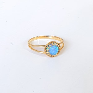 Op de afbeelding: Een gouden ring met een blauwe opaal-steen gezet in een delicaat filigraan ontwerp.