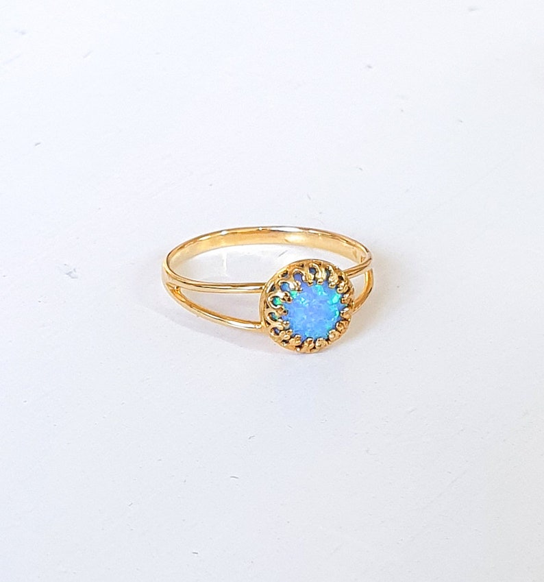 Op de afbeelding: Een gouden ring met een blauwe opaal-steen gezet in een delicaat filigraan ontwerp.