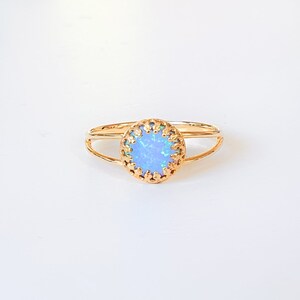 Op de afbeelding: Een delicate gouden ring met een lichtblauwe opaal-steen gezet in een decoratief filigraanontwerp.