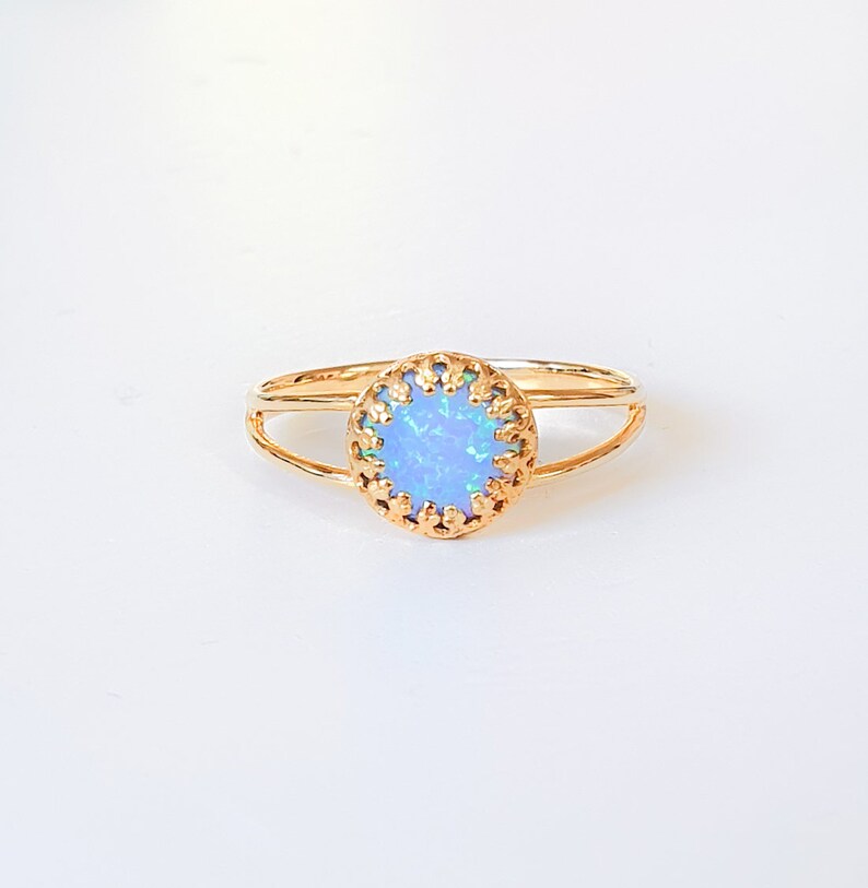 Op de afbeelding: Een delicate gouden ring met een lichtblauwe opaal-steen gezet in een decoratief filigraanontwerp.