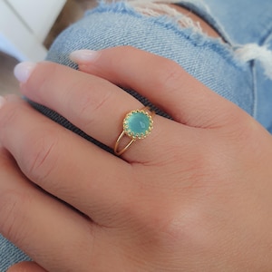 Op de afbeelding: Een gouden ring met een lichtblauwe edelsteen in een gegolfde zetting. De ring zit aan een vinger.