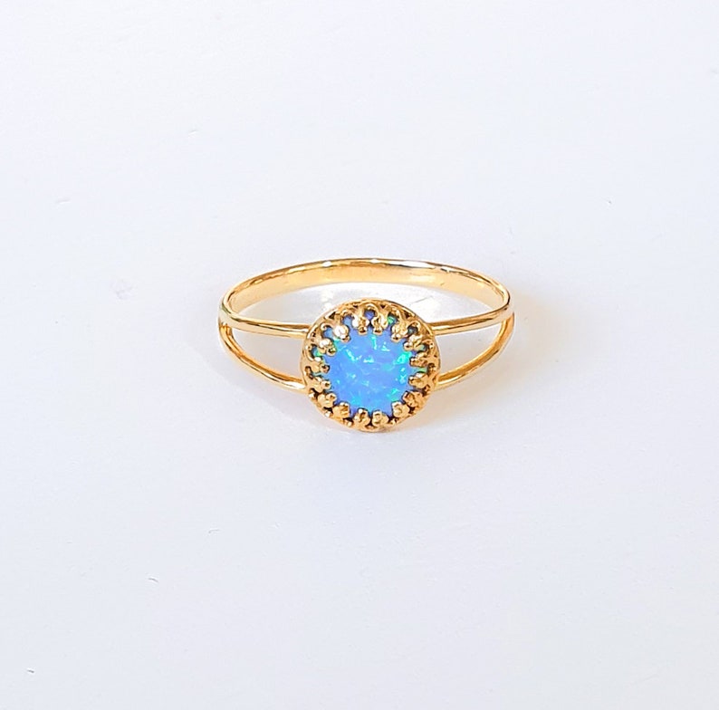 Op de afbeelding: Een gouden ring met een blauwe opaal-steen gezet in een delicaat, versierd gouden frame.