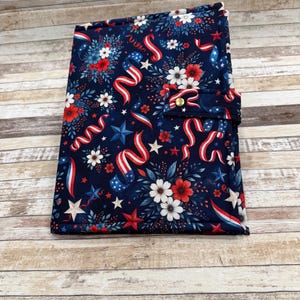 May include: A navy blue fabric notebook cover with a patriotic design. The cover features red, white, and blue ribbons, stars, and floral patterns. It has a button closure and is likely used for journaling or note-taking.