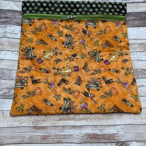 May include: A rectangular quilted pouch featuring an orange fabric with a repeating pattern of cartoon pumpkins, owls, and corn stalks. The top section is a black fabric with a green star pattern, separated by a green zipper closure.