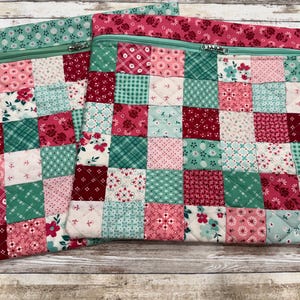 May include: Two quilted patchwork zipper pouches. The pouches feature a grid pattern of small squares in shades of pink, red, and teal, with floral and geometric prints. The zippers are a matching teal color.