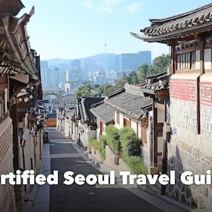May include: A narrow street in Seoul lined with traditional Korean hanok houses featuring tiled roofs and stone walls, with a modern city skyline and N Seoul Tower visible in the distance. The text Certified Seoul Travel Guide is overlaid.