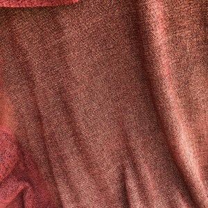 May include: Close-up of a red fabric with a textured woven pattern. The fabric has a slight sheen and is folded in a way that creates a diagonal line.