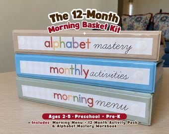 May include: A stack of three ring binders in beige, light blue, and sage green. The top binder is labeled alphabet mastery, the middle is labeled monthly activities, and the bottom is labeled morning menu. Text above reads The 12-Month Morning Basket Kit.