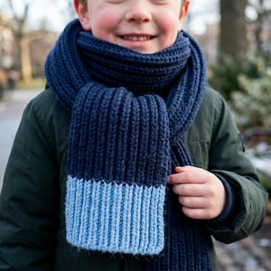 May include: A thick, ribbed knit scarf featuring a deep navy blue main section and a contrasting light blue color-blocked end. The scarf is wrapped around the neck, showcasing a textured, vertical knit pattern throughout the length.